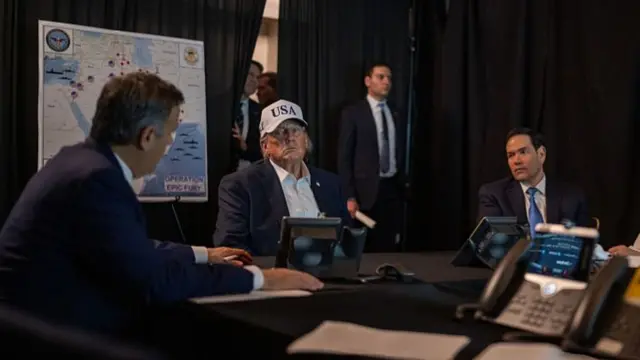 Donald Trump wearing a white USA cap whilst sitting at a table in a make-up situation room at Mar-a-Lago. Secretary of State Marco Rubio sits to his left