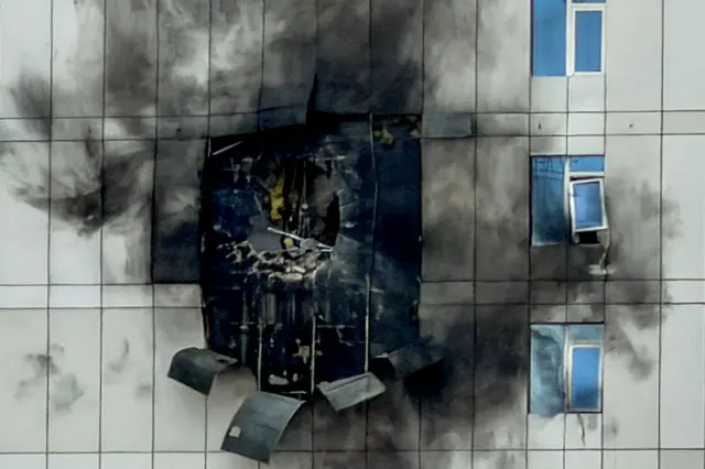 A white-panelled building with a hole in it following an Iranian strike. The panels are darkened by black soot