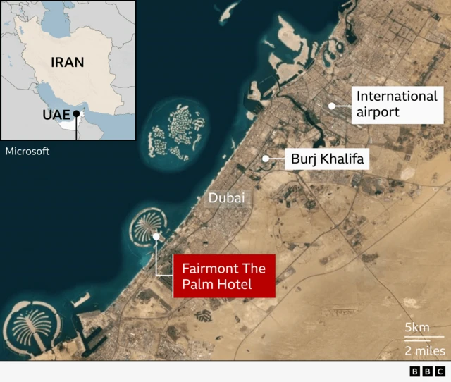 A satellite map of Dubai with the Fairmont The Palm Hotel highlighted in red on the western side of the Palm Jumeirah. Labels also mark central Dubai, the Burj Khalifa, and the international airport to the north. Two artificial palm-shaped islands are visible offshore. An inset map labels the UAE and Iran, which is just to the north across The Gulf.