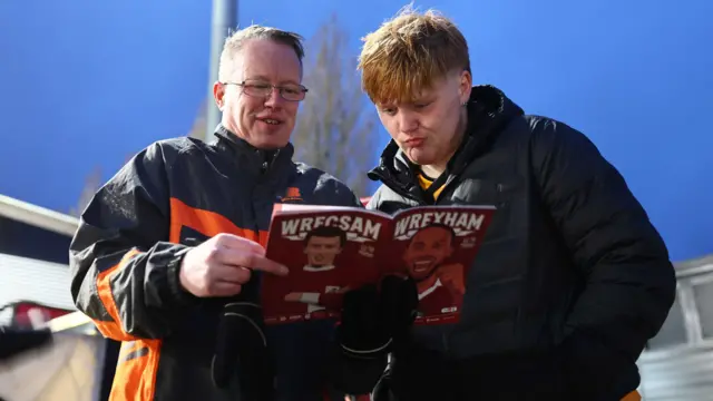 Hull City fans read the Wrexham matchday programme outside the Stok Cae Ras