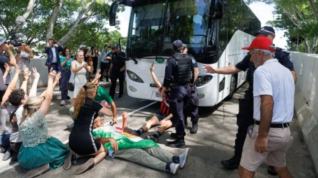 A protester draped in the Iranian flag before the Islamic revolution lays in front of a bus on the pavement in Australia in support of the Iranian women's football team