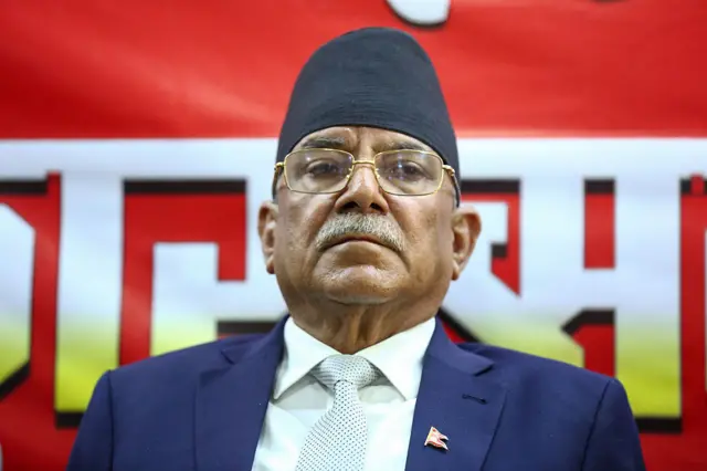 Prachanda wears a dark blue suit, shirt and polka dotted tie