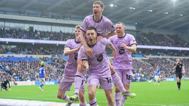 Dom Jefferies of Lincoln in a purple kit celebrates scoring his side's second goal at Cardiff with team-mates Rob Street, Conor McGrandles and Ben House