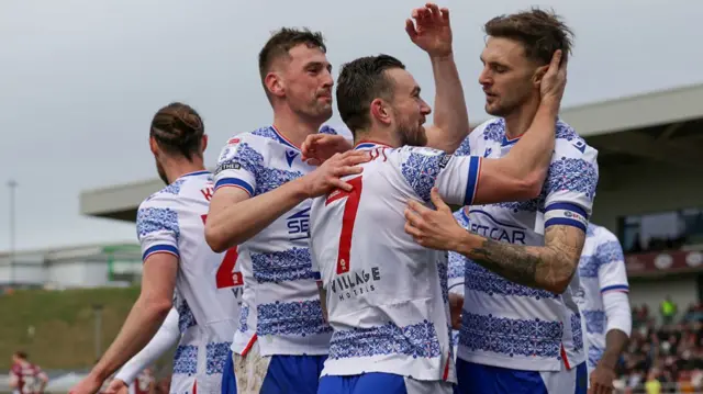 Jack Marriott in a blue and white hooped shirt and blue shorts celebrates with teammates after scoring for Reading