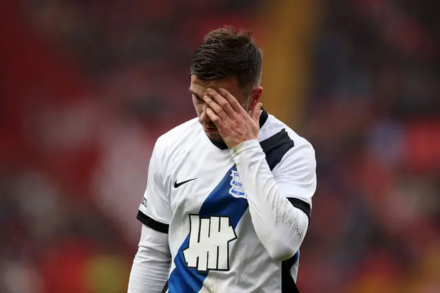 Birmingham City's Kai Wagner holds his hand to his face, dressed in a white kit with a blue sash and black rings on the sleeves