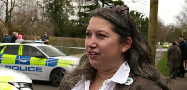 Genevieve standing on Laundry Lane. She is wearing a pair of sunglasses on her head, a white shirt and brown jacket.