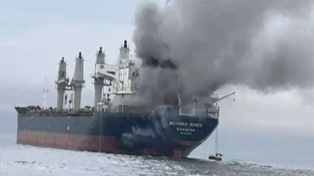 Black smoke rises from a large container ship