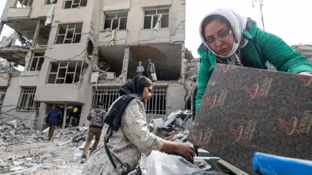 A family gathers the remaining furniture from an apartment damaged by an airstrike in Tehran
