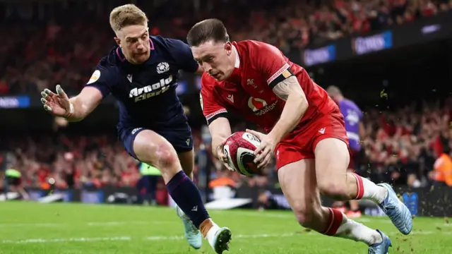 Josh Adams of Wales dives in to score his team's second try whilst under pressure from Kyle Steyn