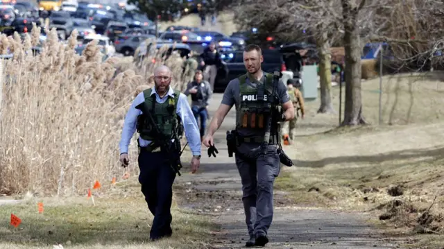 armed law enforcement officers walking on sidewalk in front of a bunch of cars