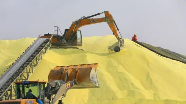 Two cranes dig a large pile of yellow powder