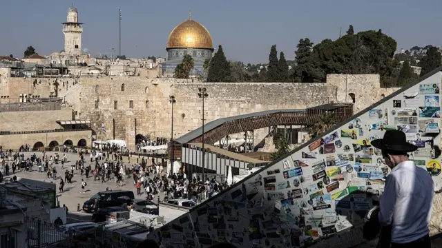 A man walks down to the Western Wall as the Dome of the Rock at the Al-Aqsa mosque compound appears in the background