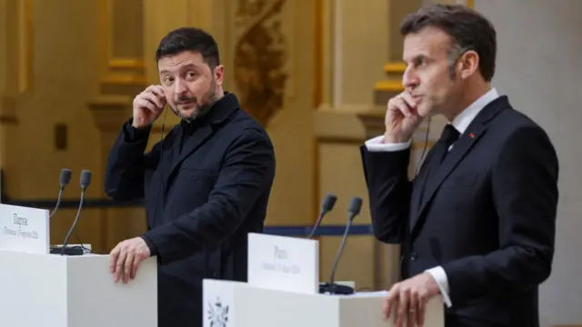 Ukraine's President Volodymyr Zelensky (L) and France's President Emmanuel Macron (R) put on a earpiece as they deliver a speech during a joint press conference