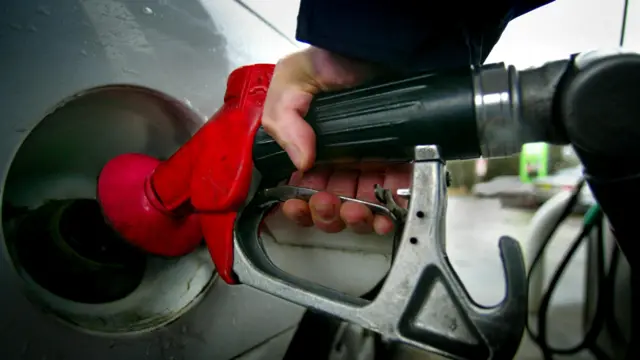 A close up of a motorist filling a car with a red fuel pump at a petrol station.