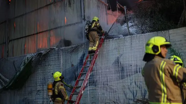 Firefighters climb a ladder into a building on fire