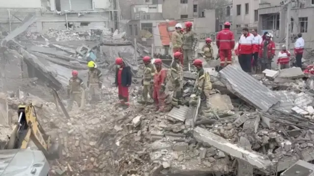 Iranian Red Crescent aid workers and firefighters work at a residential site damaged by strikes, in Javadiyeh district, Tehran, Iran.