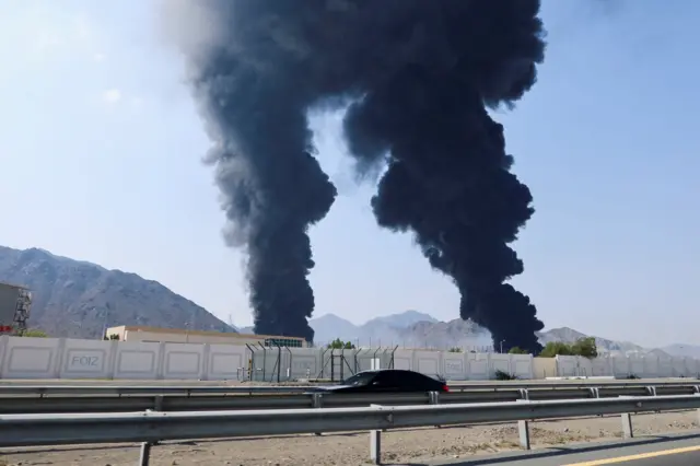 Two parallel clouds of black smoke billow into the sky from an area near the port of Fujairah