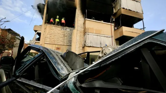 Rescue workers inspect a burnt out building in front of the wreckage of a car