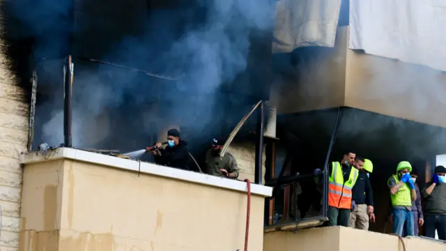 A close-up of the building, where rescuers can be seen working as thick smoke billows from the balconies