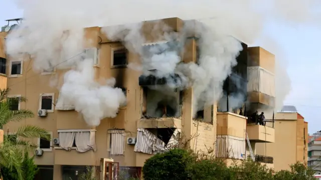Smoke pours out of at least six winds in an apartment block. The block has been partially obscured by the smoke and the outside of a section of the building has been charred
