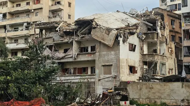 A several story building that has taken extensive damage, with the roof caved in and walls falling down. Rubble is strewn on the ground outside