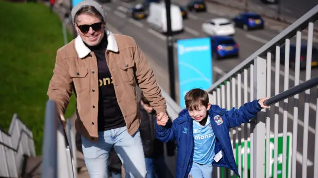 A young Coventry fan holds the hand of his dad as he walks up the steps at the CBS Arena