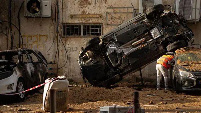 Debris is scattered around a crater and damaged cars after a projectile impact on March 15, 2026 in Holon, Israel.