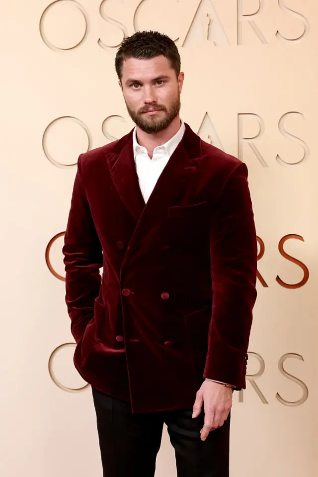 Chase Stokes poses for a photo in a red velvet suit