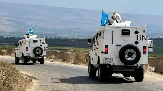 Two white vans drive along a road