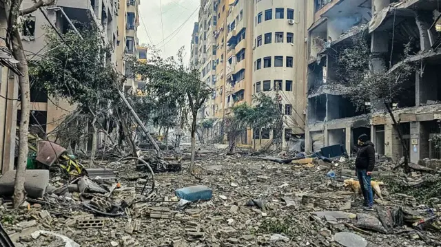 A man and his dog walk across the rubble of a building at the site of an Israeli airstrike in Beirut's southern suburb Haret Hreik.
