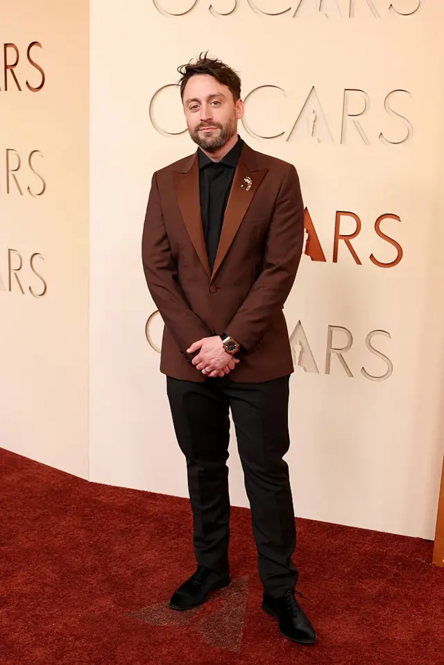 Kiernan Culkin in a maroon suit jacket with a black shirt and black pants