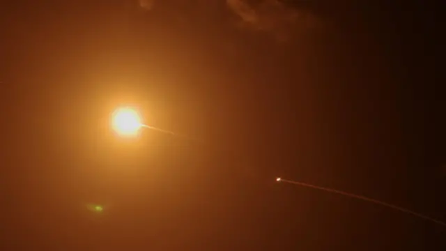 Streaks of light illuminate the sky with a bright yellow circle during a missile interception.