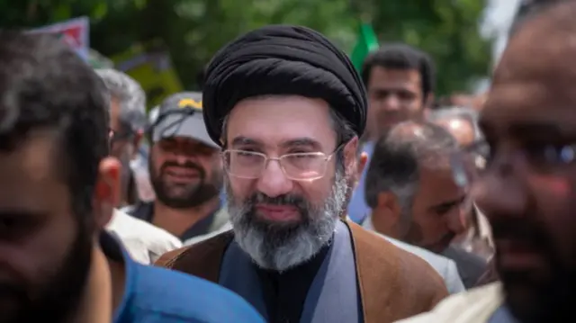 Stock picture of Mojtaba Khamenei in black turban, brown cloak and grey suit as he walks among crowd