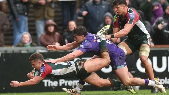 Billy Searle (left) dives over the line as an Exeter player tries to tackle him from behind and a Leicester team-mate stands behind them