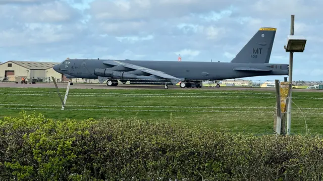 A b-52 plane is seen behind barbed wire and a hedge at RAF Fairford