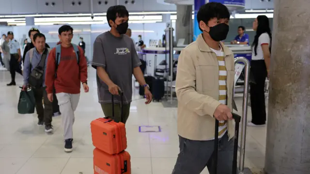 Thai crew members arrive at Suvarnabhumi International Airport in Bangkok, Thailand, wheeling suitcases and wearing black face masks.