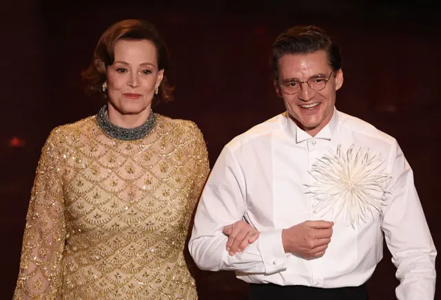 Sigourney Weaver and Pedro Pascal walk on stage linking arms