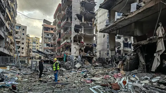 Men standing around in piles of rubble amid destroyed and damaged buildings