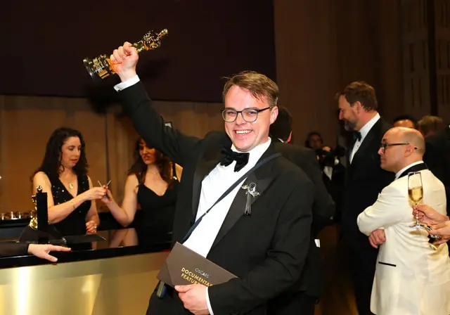 Russian teacher Pavel Talankin hoists his Oscar for Best Documentary Feature Film, smiling.