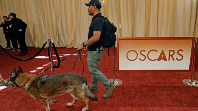 A security officer with a dog on the red carpet, next to the 'Oscars' sign.