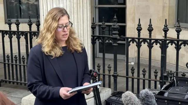 A woman with long fair hair reads a speech to the media outside a court building