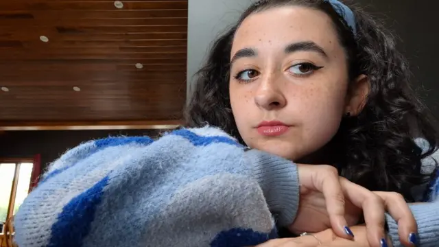 A girl with lipstick and eye make-up up close. She has black curly hair and faint freckles on her cheeks.