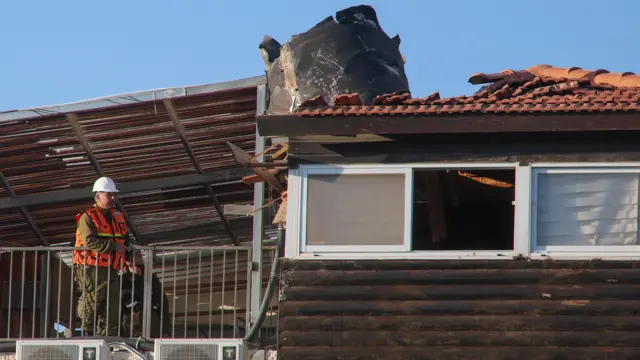 A piece of shrapnel sticks out of a rood as a worker looks on