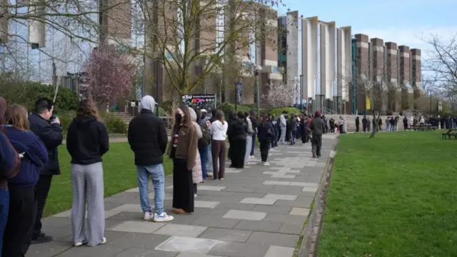 A queue of students wearing face masks line up on the campus