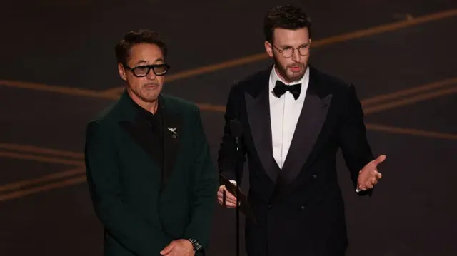 Chris Evans and Robert Downey Jr stand on stage in front of a microphone