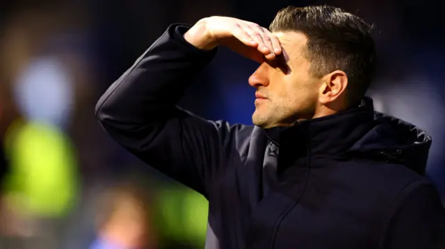 John Mousinho shields his eyes from the glare of the floodlights