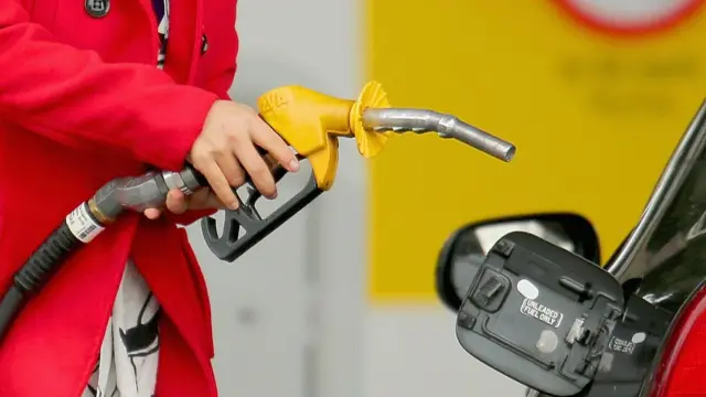 Partial view of person holding a petrol pump about to put it into the tank in a car
