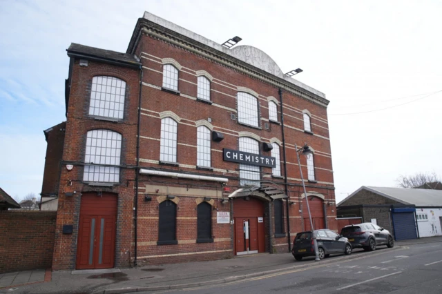 Brick building hosting a nighclub, the sign Chemistry features at the top of the main door, two cars parked slightly to the left of the entrance