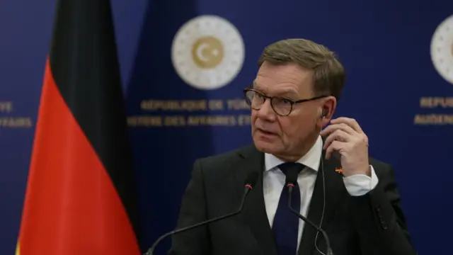 German Minister for Foreign Affairs Johann David Wadephul attends a joint press conference. He is seen putting a microphone into his ear and getting ready to speak into a microphone at a podium