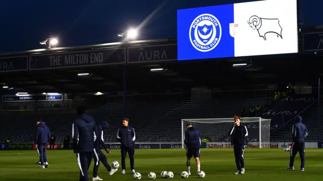 Derby players on the pitch at Fratton Park with the scoreboard showing the crests of Portsmouth and Derby